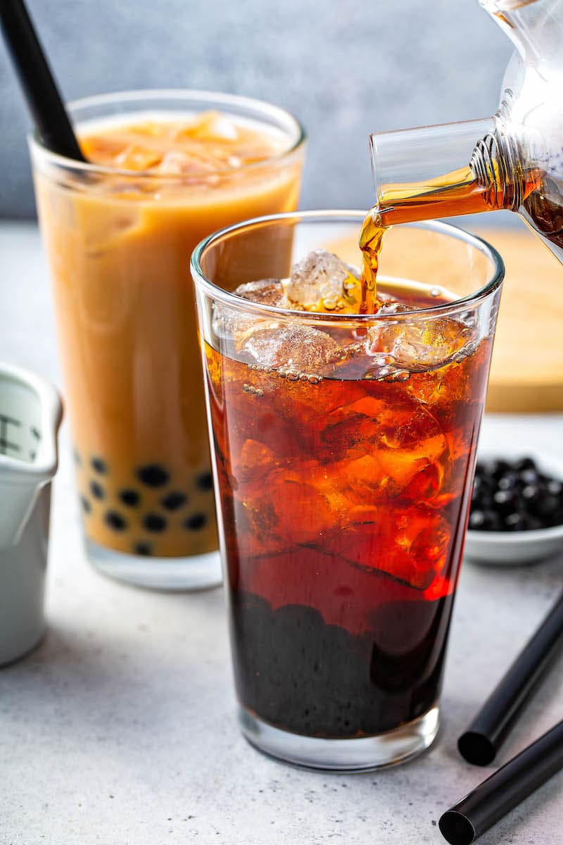 Tea being poured over ice in a tall glass. 