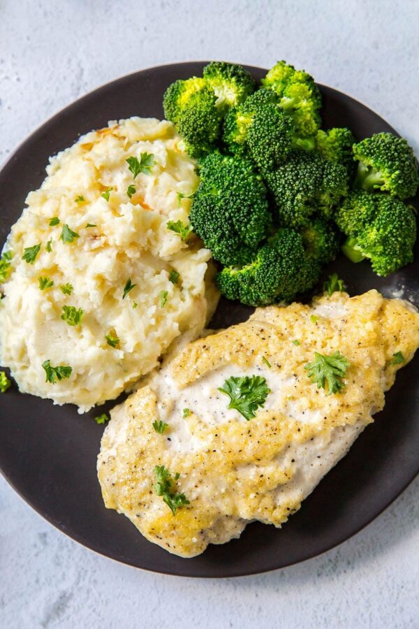 Creamy Parmesan Chicken breasts on a plate with broccoli and mashed potatoes.