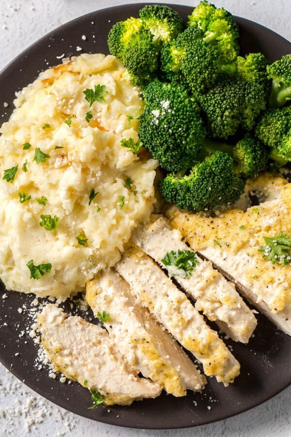 Creamy Parmesan Chicken on a black plate with sides cut into slices.