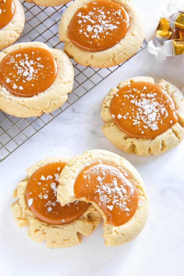 Salted Caramel Cookies with a bite taken out of one and more stacked on a cooling rack.