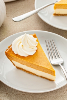 Whipped cream is piped on top of a slice of pumpkin pie cheesecake.