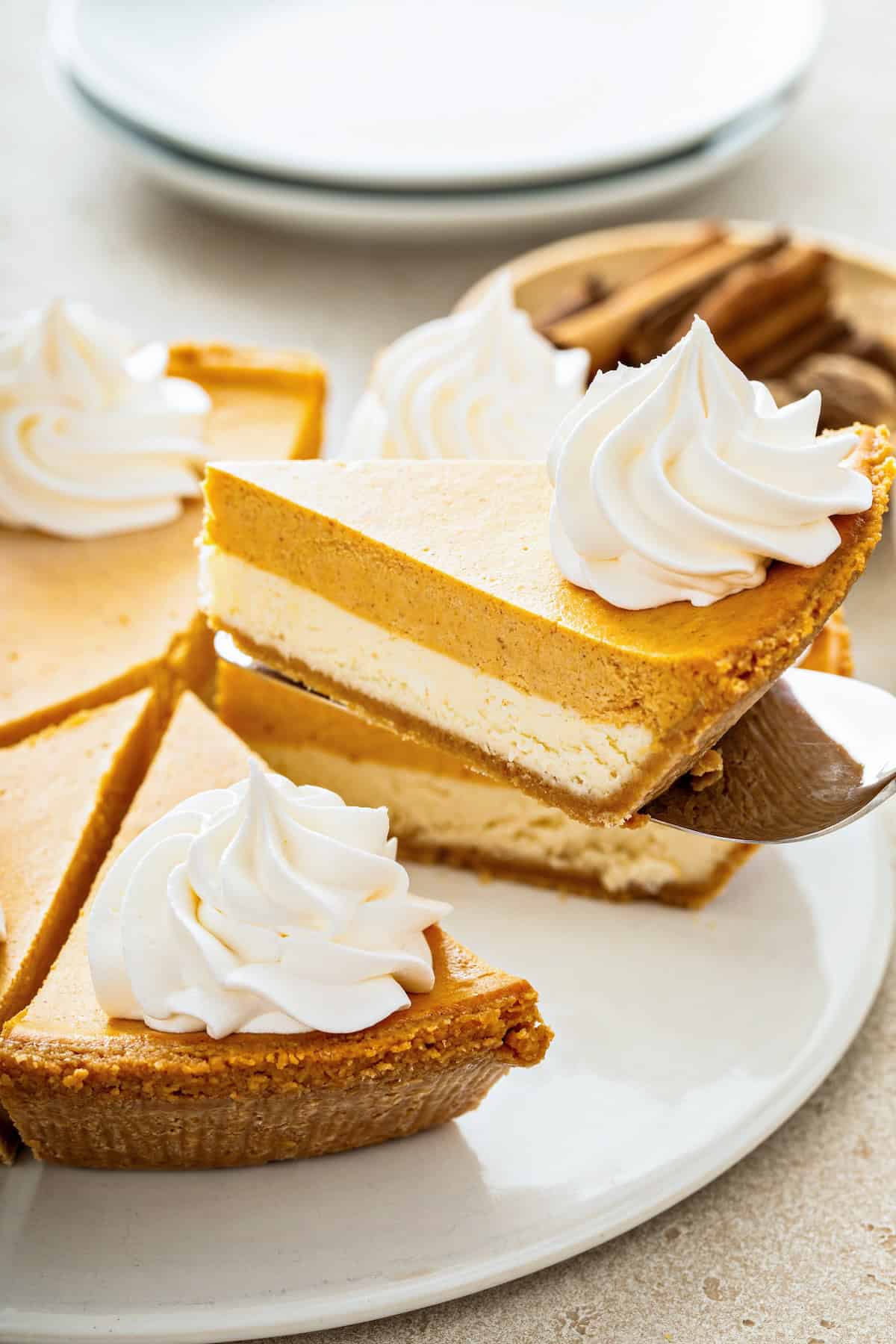 A slice of sweet pumpkin pie cheesecake is being lifted from a serving plate.