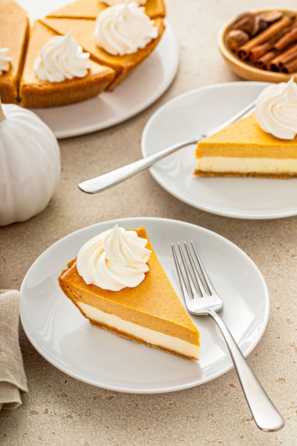 Fluffy whipped cream is piped on top of several slices of pumpkin pie cheesecake.