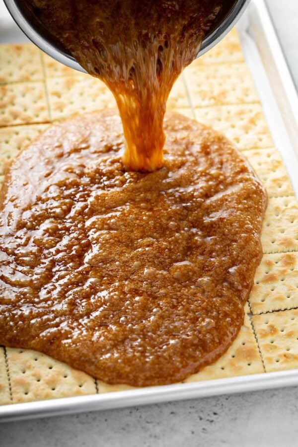 Saltine crackers on a pan with toffee being poured on top of them for Christmas Crack.