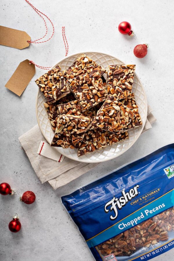 Christmas crack on a white plate next to a bag of pecans.