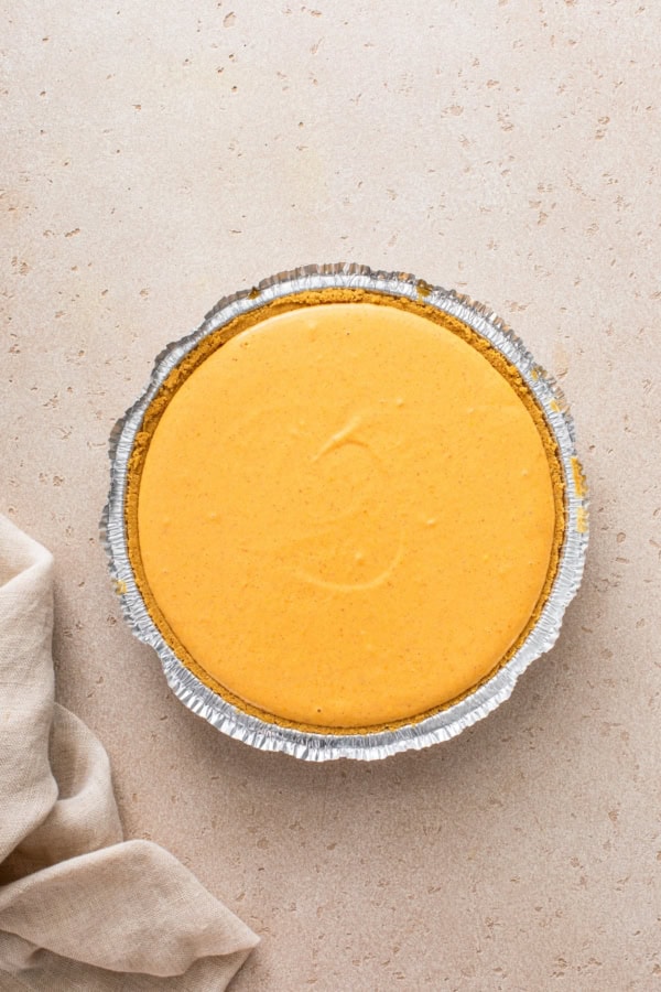 Pumpkin pie layer is presented on top of a cheesecake layer in a pie dish.