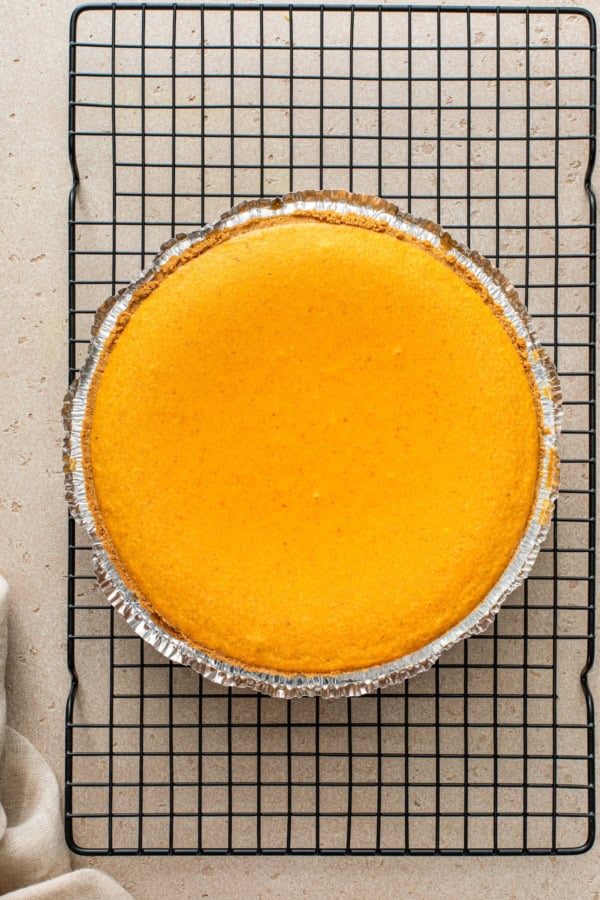 Baked cheesecake pumpkin pie recipe cooling on a wire rack.