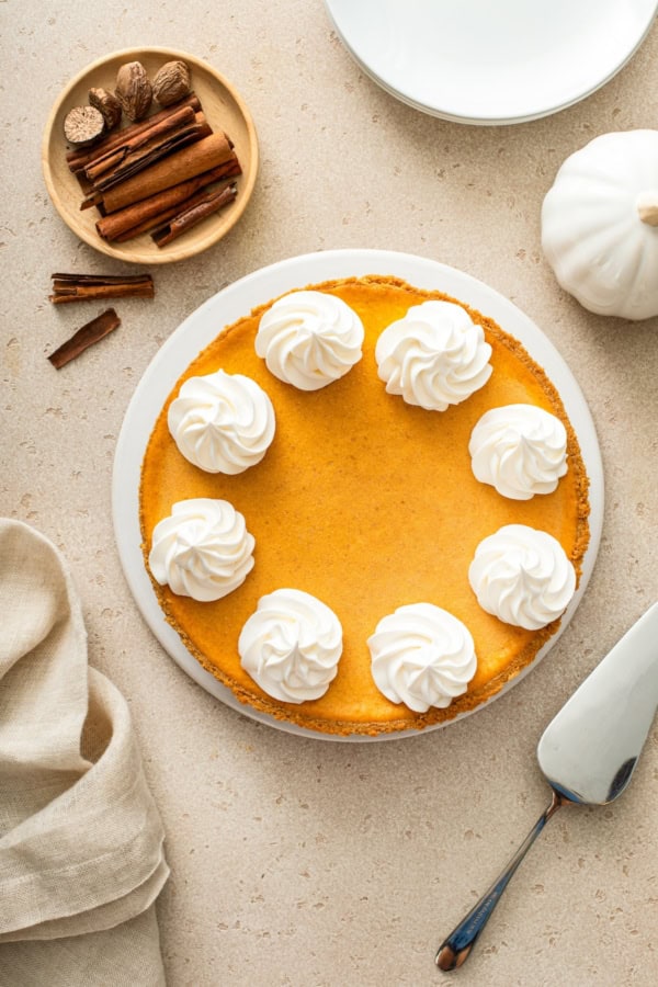 Whipped cream is piped on top of a whole pumpkin pie cheesecake.