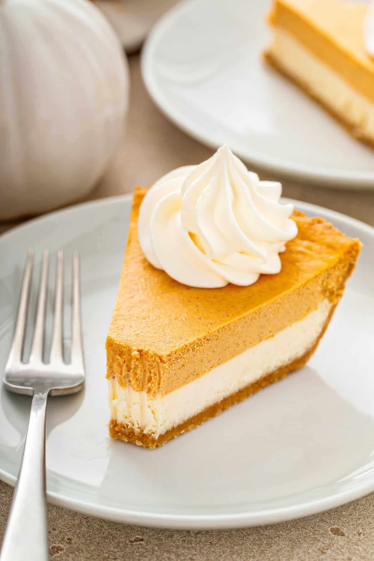 This easy Pumpkin Pie Cheesecake has a hidden cheesecake layer under the spiced pumpkin. Just ONE bowl of batter and no water bath needed! A slice of pumpkin pie cheesecake topped with whipped cream on a plate with a bite taken out of it.