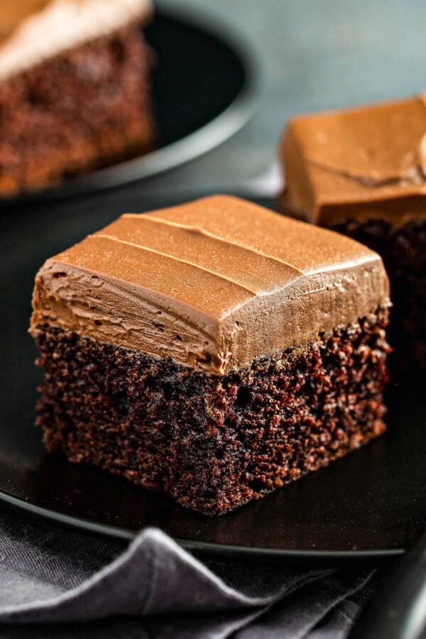 Chocolate Mayonnaise Cake on a black plate with fluffy whipped chocolate icing on top. 