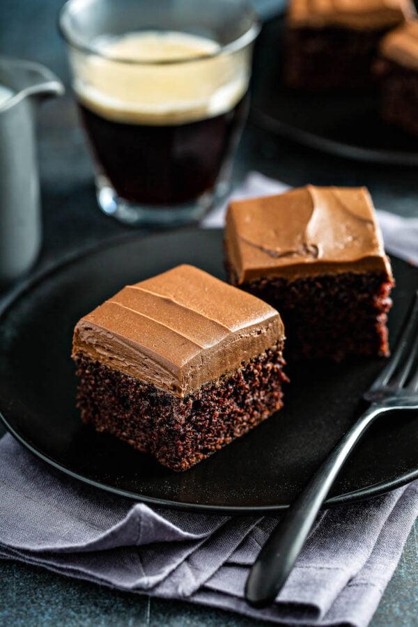 Two slices of Chocolate Mayonnaise Cake on a black plate with a fork.