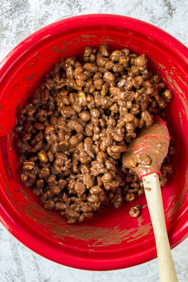 Cereal is being mixed with a chocolate peanut butter mixture in a red bowl.