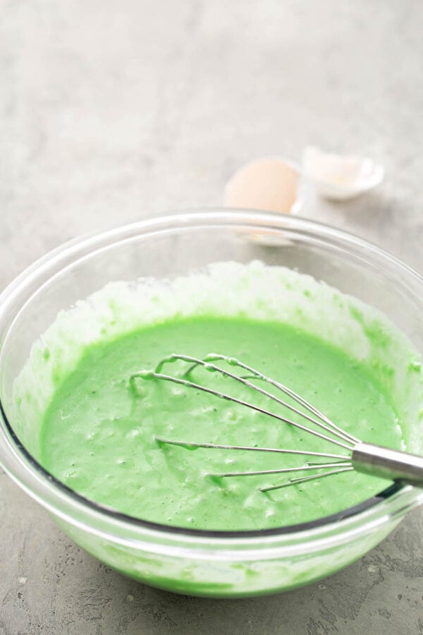 A bowl of Grinch Pancake batter in a glass bowl with a whisk.