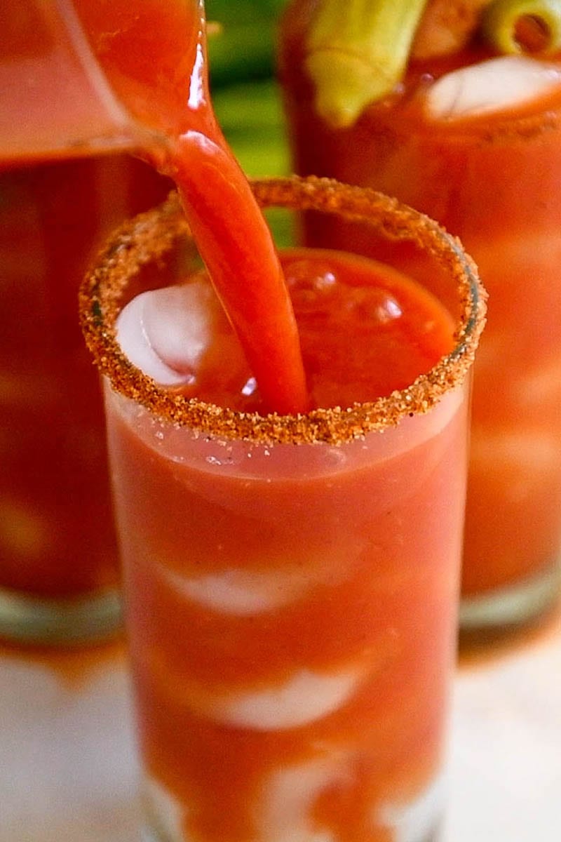 Bloody Mary Recipe being poured into a glass rimmed with cajun seasoning.