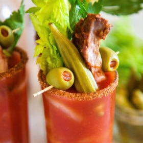 A fully loaded Bloody Mary mix with olive, okra, and pork rib garnishes on top.