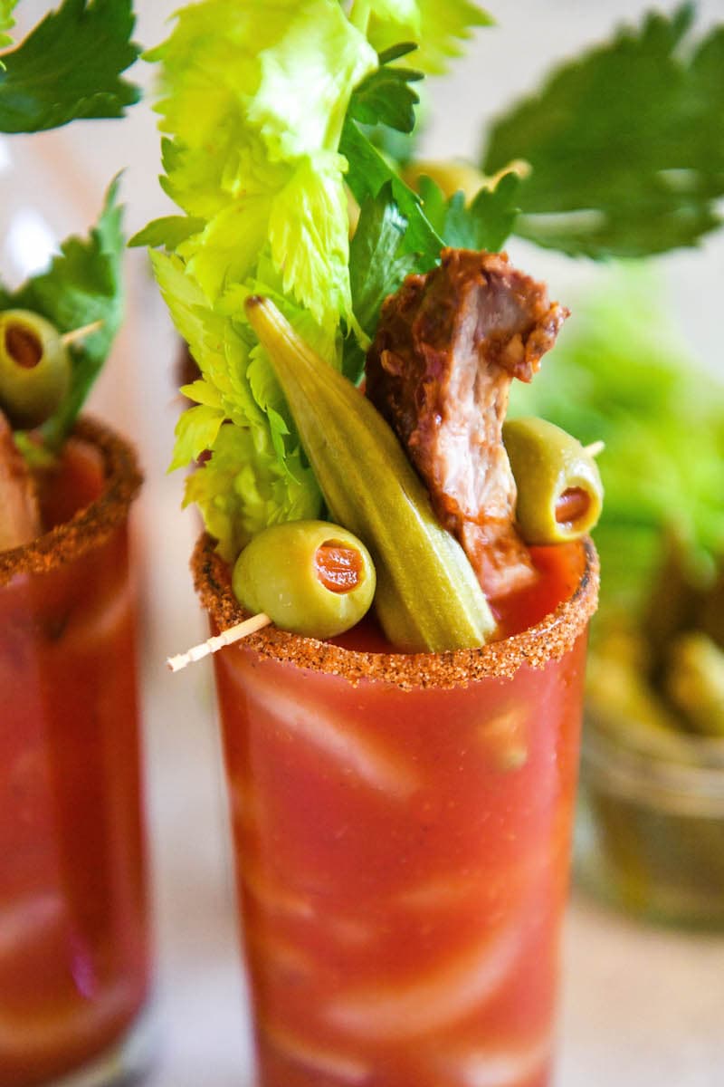 A fully loaded Bloody Mary mix with olive, okra, and pork rib garnishes on top.