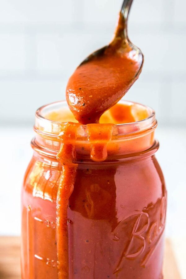 Homemade Enchilada Sauce in a clear jar with a spoon.
