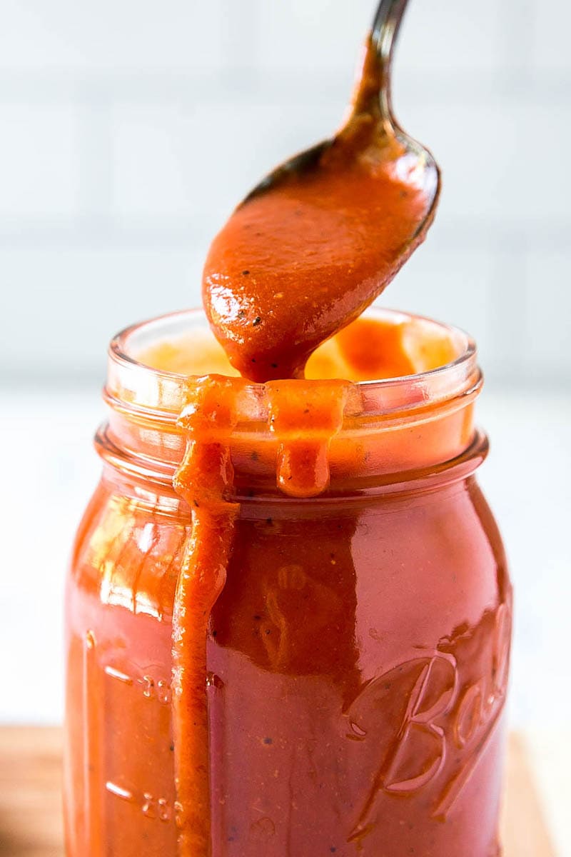 Red enchilada sauce in a glass jar with a spoon.