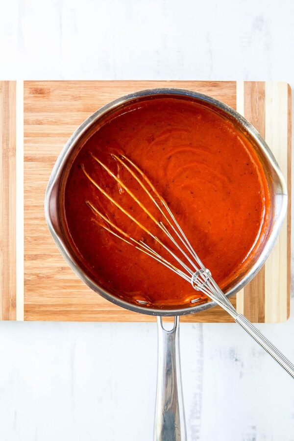 Red Enchilada sauce in a pot on a cutting board.