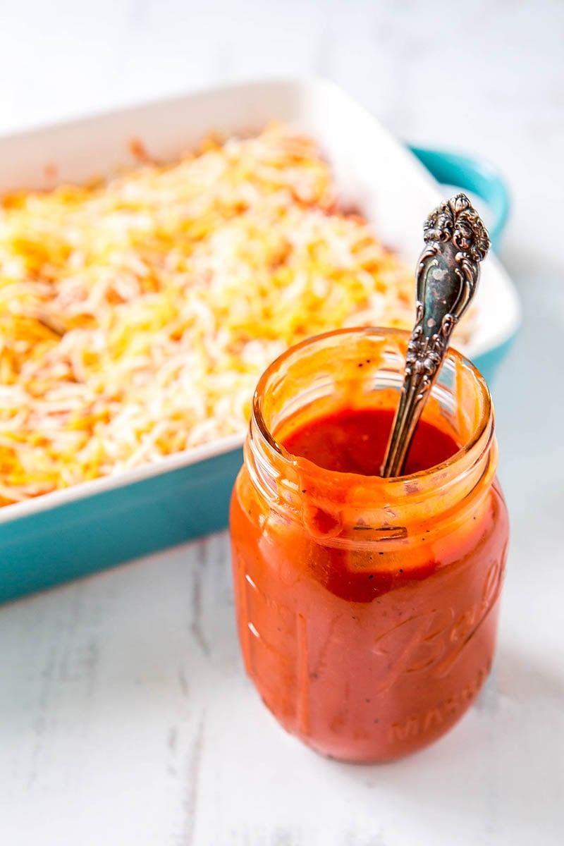 Homemade enchilada sauce in a mason jar with a dish of enchiladas in the background.