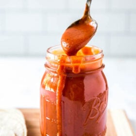 Homemade enchilada sauce recipe in a jar with a spoon scooping some out.