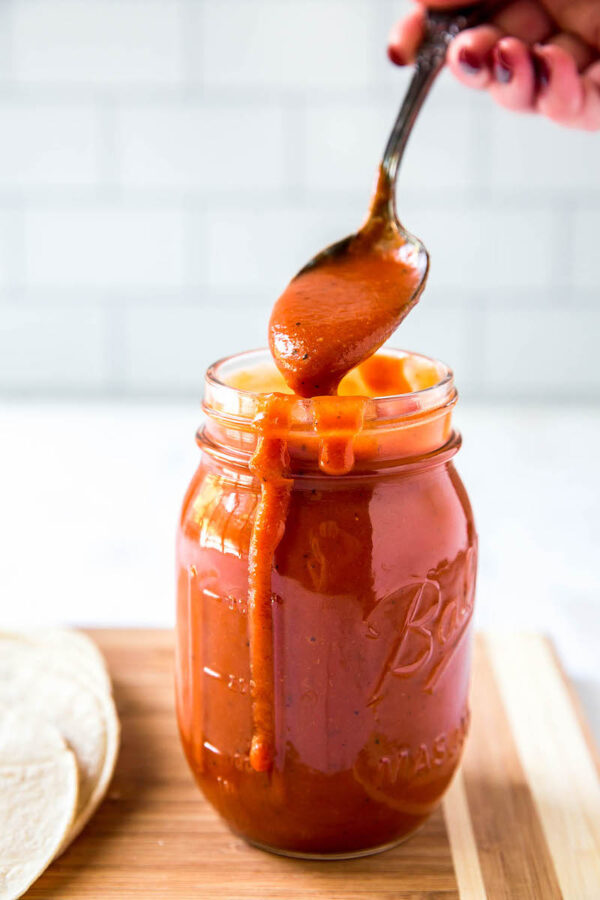 Homemade enchilada sauce recipe in a jar with a spoon scooping some out.