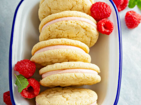 Raspberry Cream Sugar Cookie Sandwiches in a white bowl with fresh raspberries