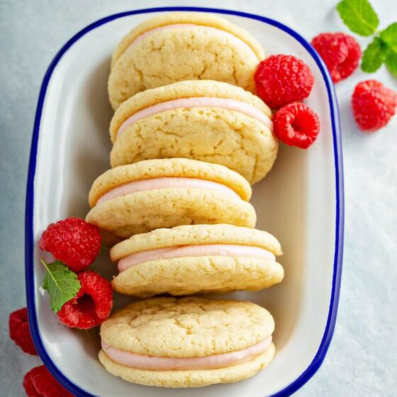 Raspberry Cream Sugar Cookie Sandwiches in a white bowl with fresh raspberries