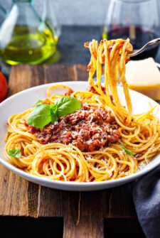 Spaghetti bolognese in a bowl with a fork taking a bite out of it.