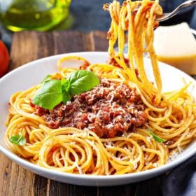 Spaghetti bolognese in a bowl with a fork taking a bite out of it.