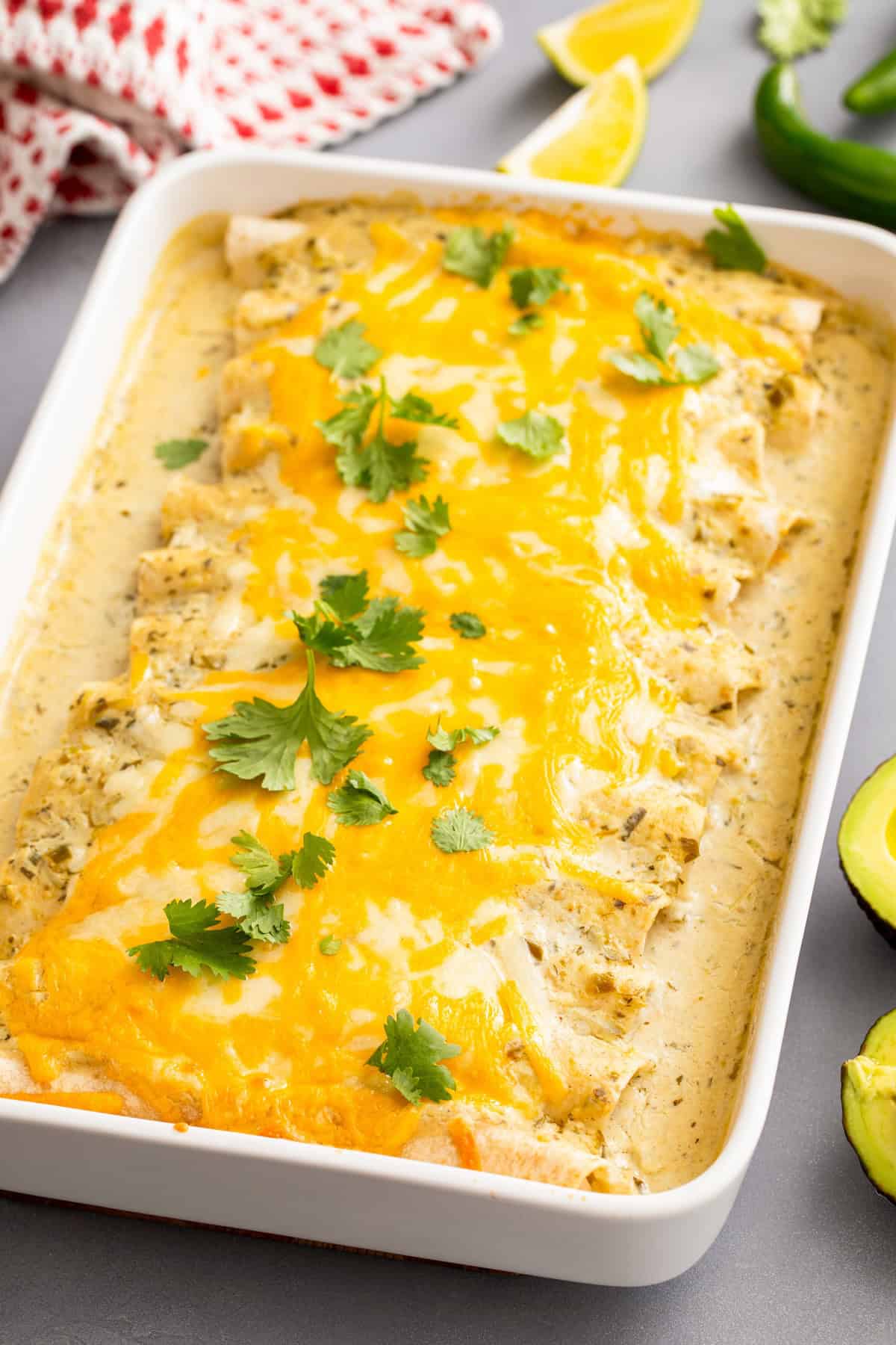 Cheesy, creamy white chicken enchiladas with lots of melted cheese on top in a large white casserole dish with fresh cilantro on top.