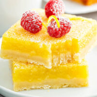 Lemon Bars stacked on top of each other on a white plate with a bite taken out of one.