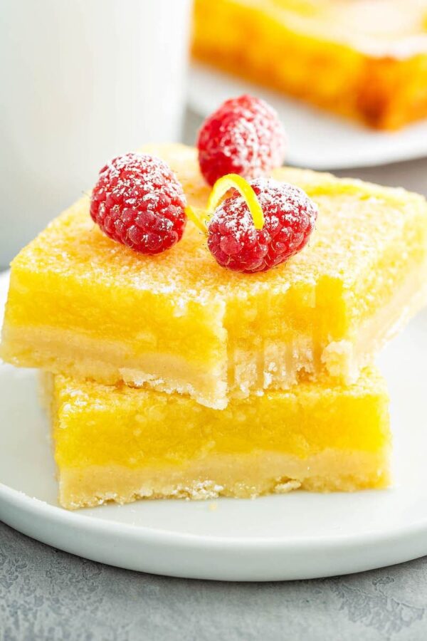Lemon Bars stacked on top of each other on a white plate with a bite taken out of one.