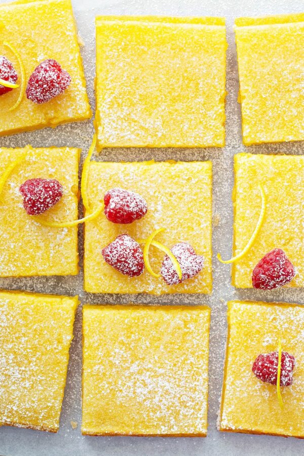 Lemon bars on parchment paper with raspberries on top. 