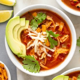 Avocados, cheese, crispy tortilla strips, and fresh cilantro garnish a full bowl of tortilla chicken soup.