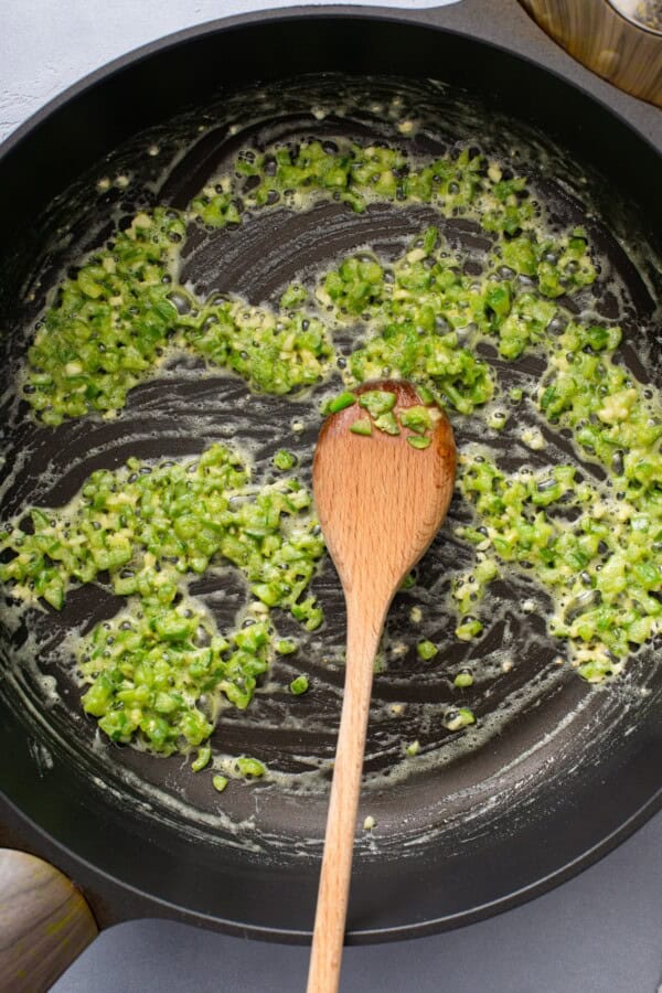 Green chile mixture cooking in a skillet with a wooden spoon.