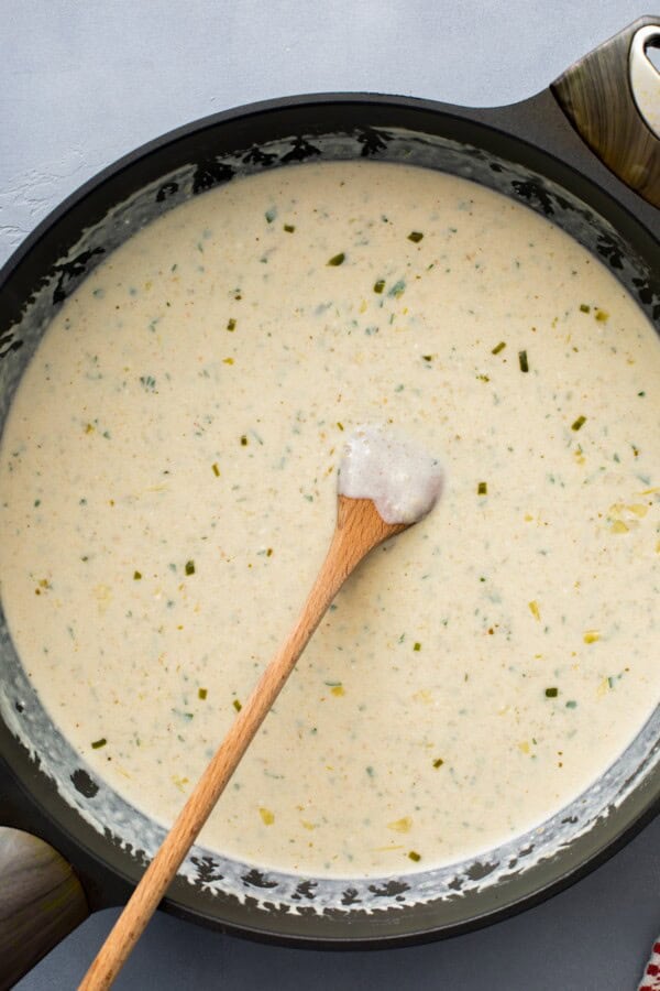 Creamy white enchilada sauce is being mixed in a skillet.