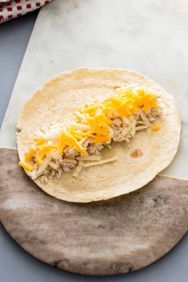 A single tortilla is filled with cooked shredded chicken, onions, and shredded cheese.