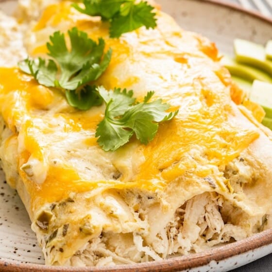 Sliced avocados are placed beside a serving of sour cream chicken enchiladas.