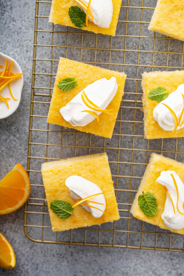 Slices of orange coconut cake cut into squares with whip cream.