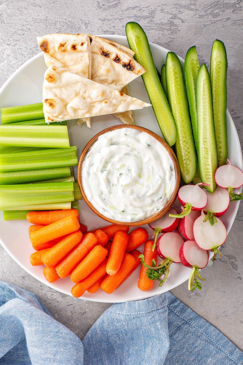 A bowl of Greek Tzatziki Sauce surrounded by carrots, celery, pita bread and other foods for dipping