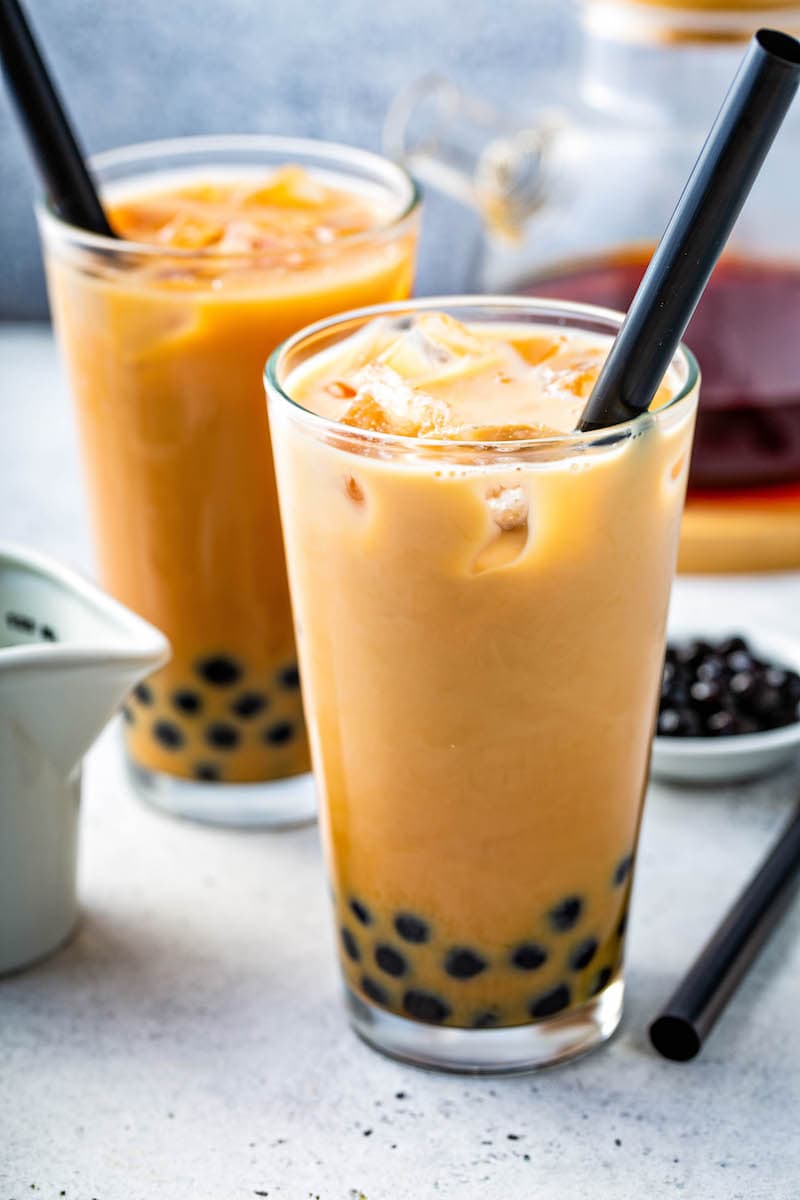 two glasses of Bubble Tea with black tapioca balls and a black straw. 