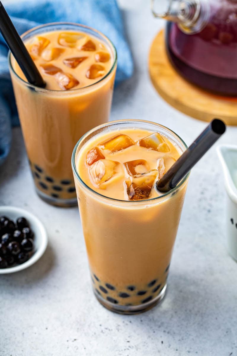 Up close image of Bubble Tea in a clear glass with ice on top and a black straw.