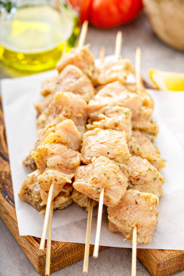 Stacks of wood skewers with pieces of marinated raw chicken breasts on them.