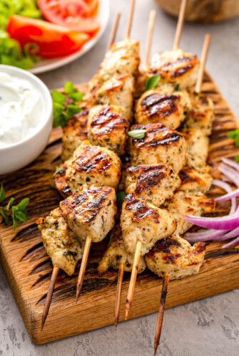 Stack of wooden skewers with cooked chicken souvlaki next to a bowl of dipping sauce
