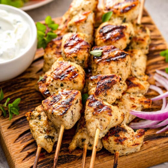 Stack of wooden skewers with cooked chicken souvlaki next to a bowl of dipping sauce