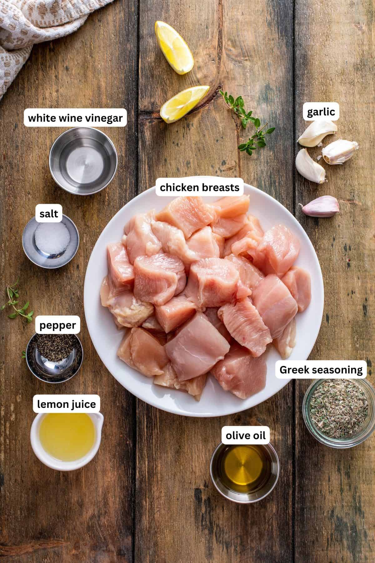 The ingredients for chicken souvlaki recipe in order from top to bottom: white wine vinegar, salt, chicken breast, garlic, pepper, lemon juice, olive oil, Greek seasoning.