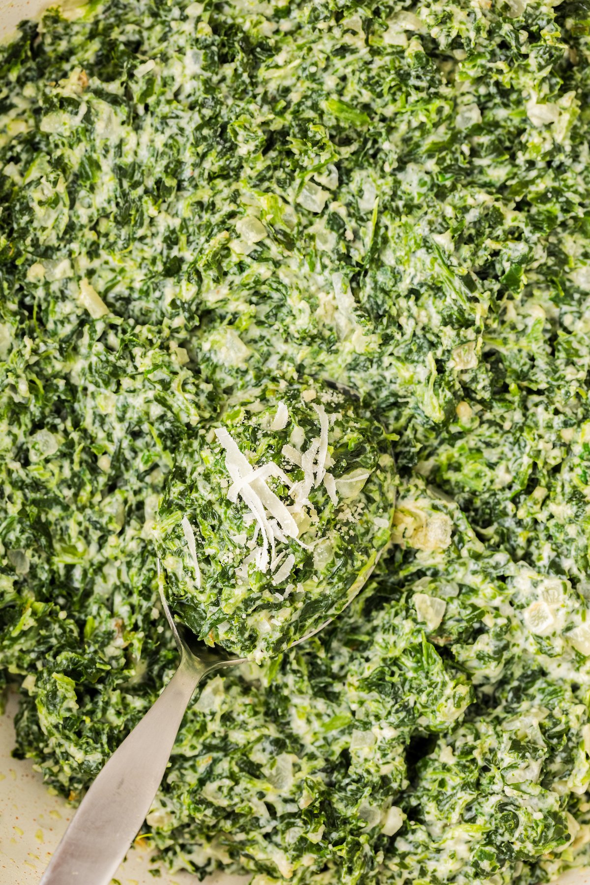 Close-up of the best creamed spinach in a skillet with a serving spoon scooping out a serving.