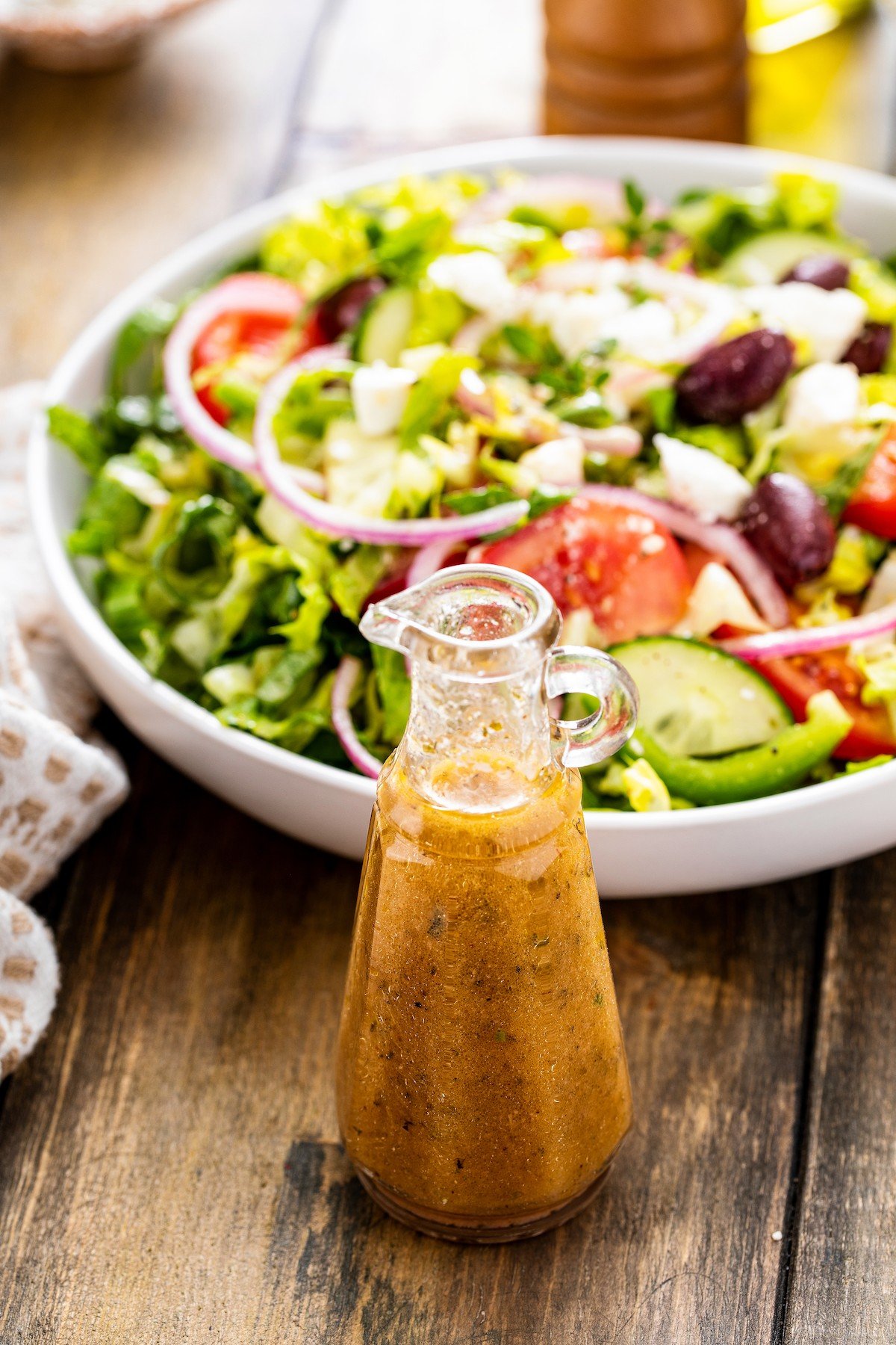 Container of salad dressing in front of a Greek salad.