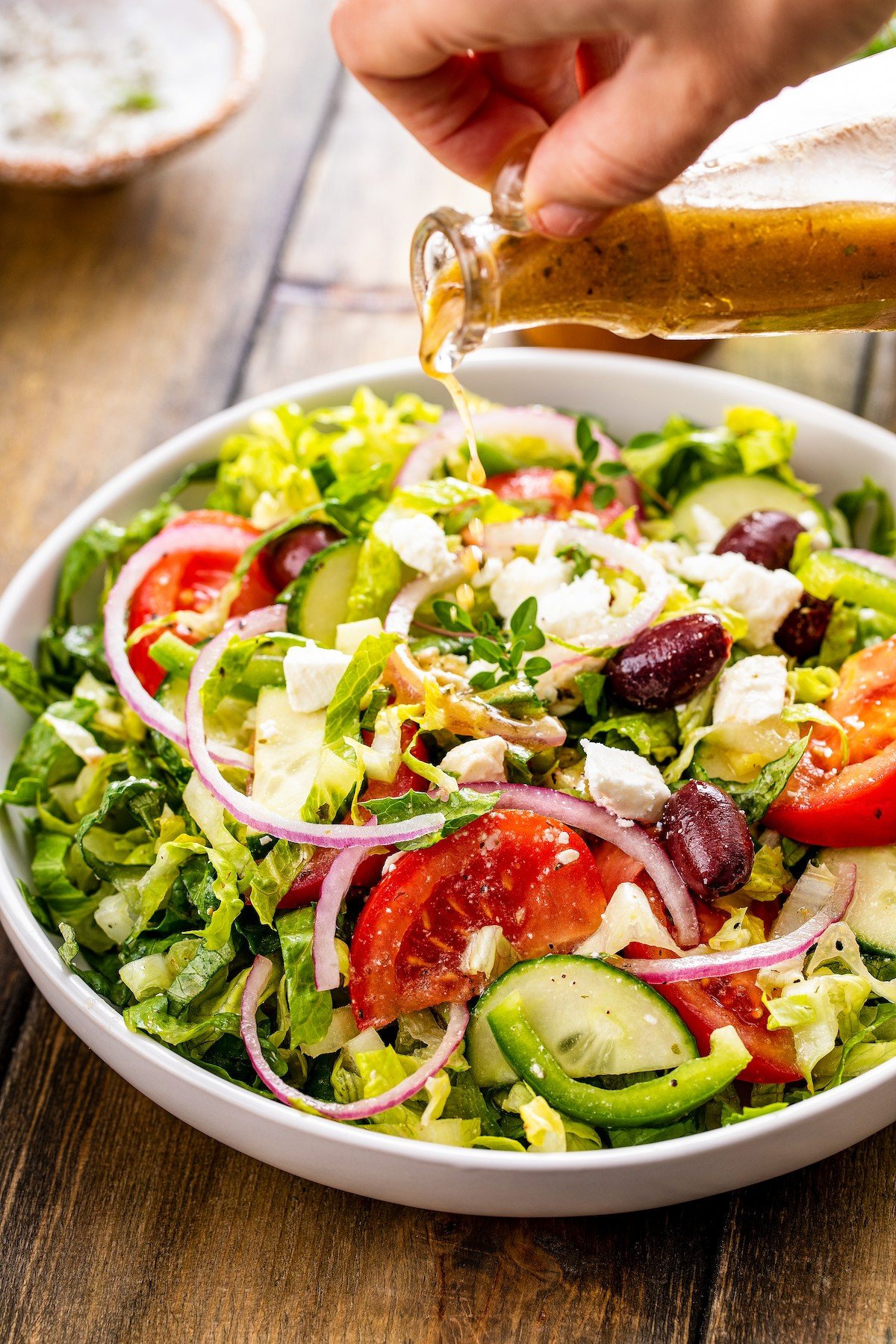 Dressing poured over lettuce, red onion, tomatoes, feta cheese, and more.
